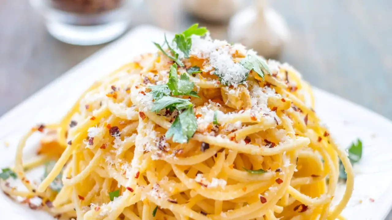 Pyszne spaghetti aglio olio, posypane parmezanem i natką pietruszki, z płatkami chili w tle.