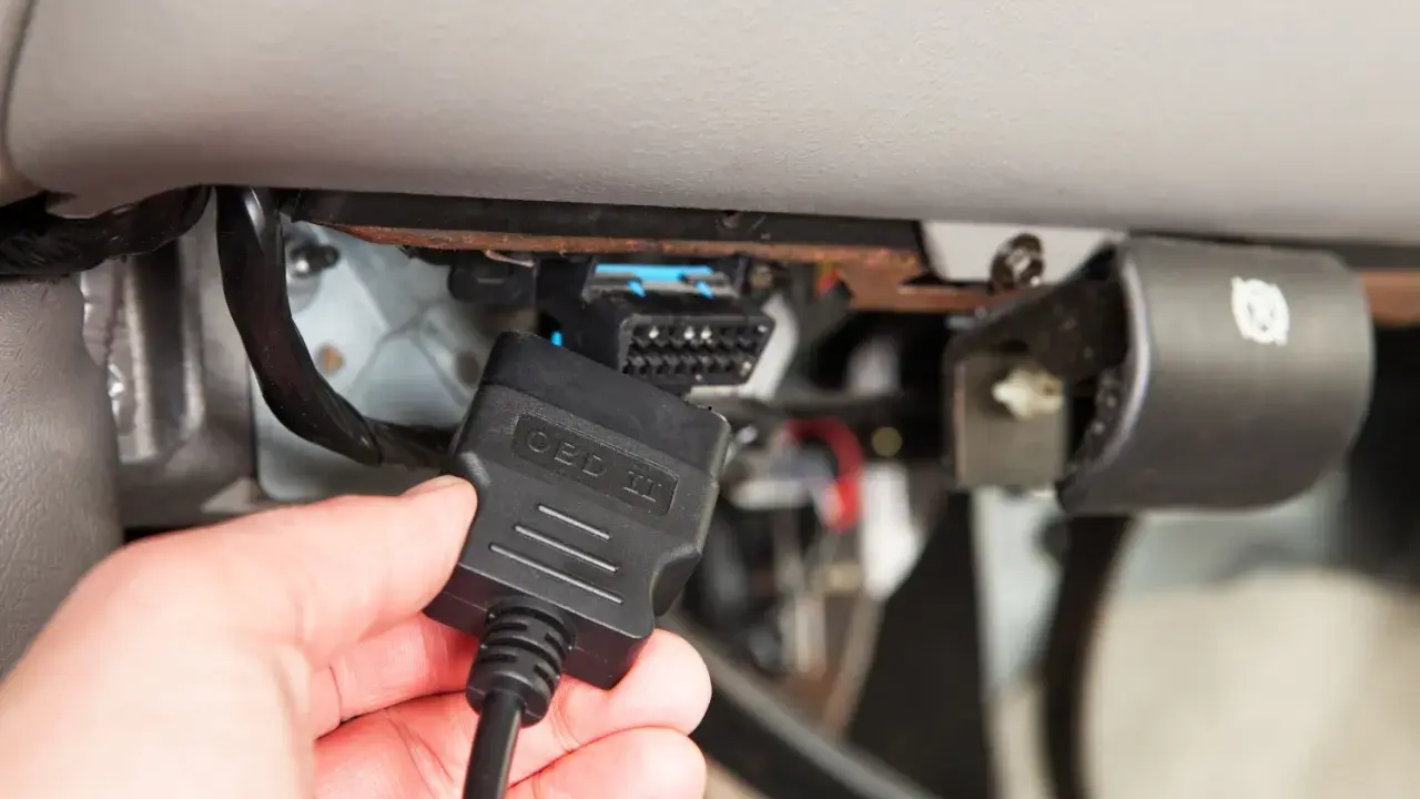 Ręka podłącza kabel OBD II do złącza diagnostycznego pojazdu, aby sprawdzić błędy DTC.