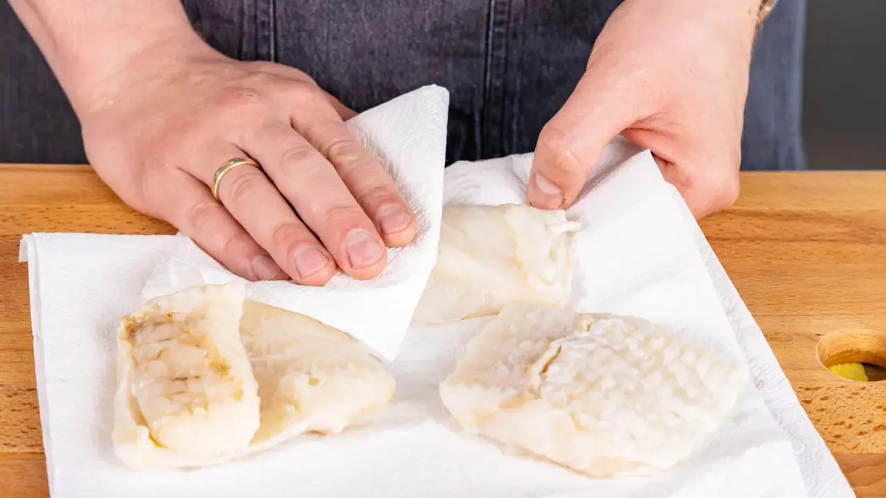 Hände tupfen Steinbeißer Fischfilets auf Küchenpapier trocken, bereit für die Zubereitung.
