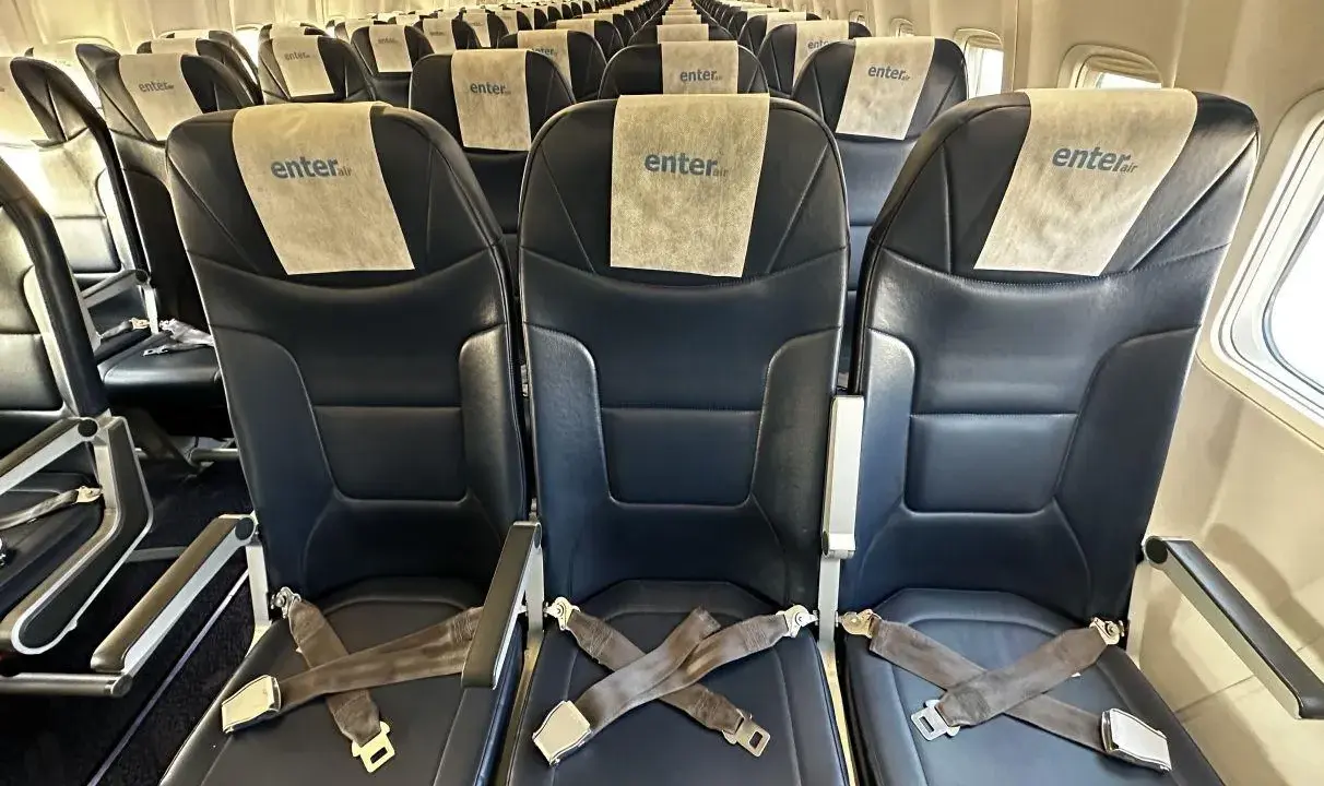 Puste, ciemne fotele w samolocie Enter Air z pasami bezpieczeństwa.