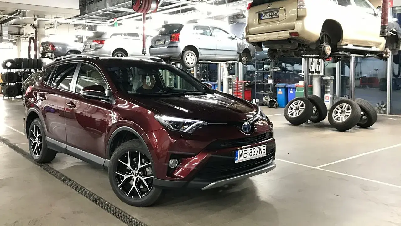 Czerwona Toyota RAV4 w serwisie. W tle inne auta na podnośnikach. Zastanawiasz się nad toyota trzeci przegląd gwarancyjny cena?