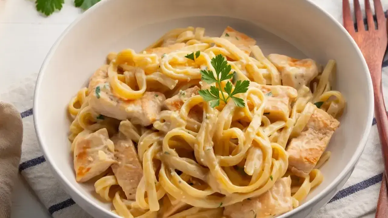 Pyszne makaron tagliatelle z kurczakiem w kremowym sosie, udekorowane natką pietruszki. Idealne danie na obiad.