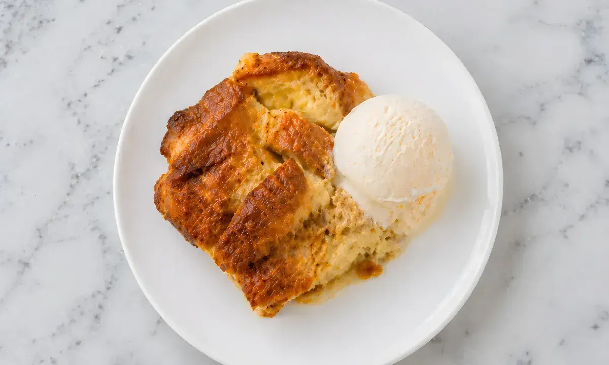 Un délicieux pain perdu au four, doré et moelleux, servi avec une boule de glace à la vanille sur une assiette blanche.