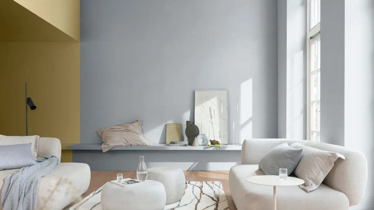 Sala de estar con paredes en tonos grises y mostaza, muebles claros y alfombra con diseño orgánico. Ideales colores suaves para pintar una casa.