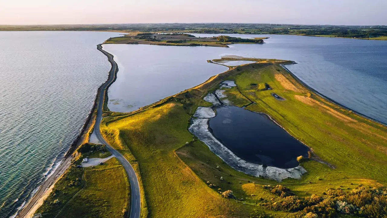 Grönskande landskap med en slingrande väg längs kusten i Danmark. En vy som från ett utkikstorn Danmark, med vatten och fält.