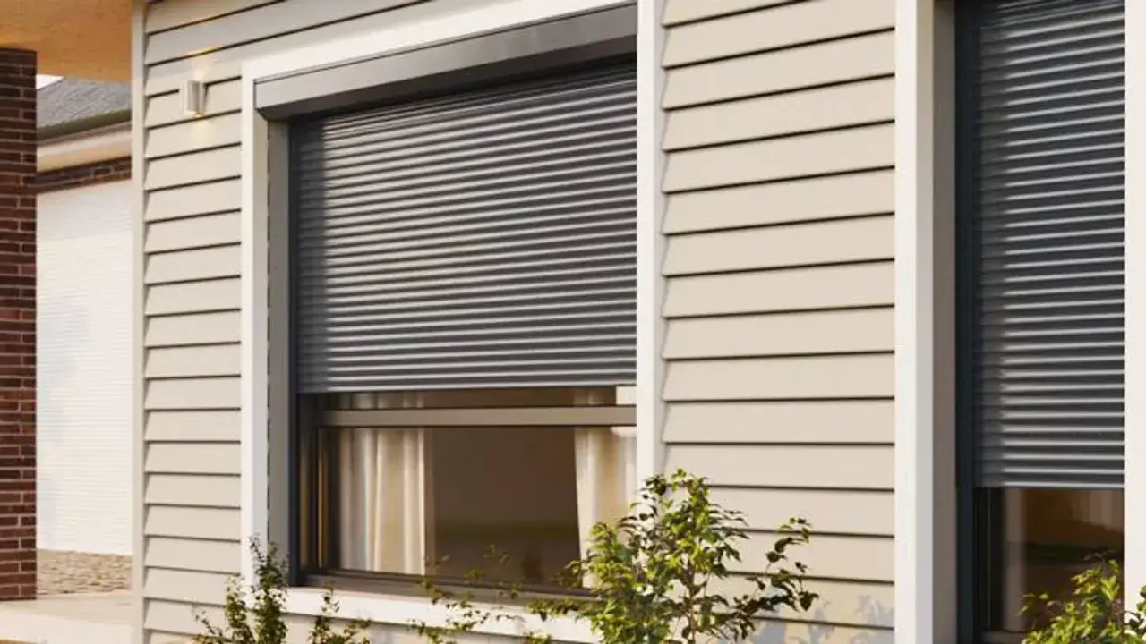 Volet roulant gris fermé sur une fenêtre de maison avec bardage beige.