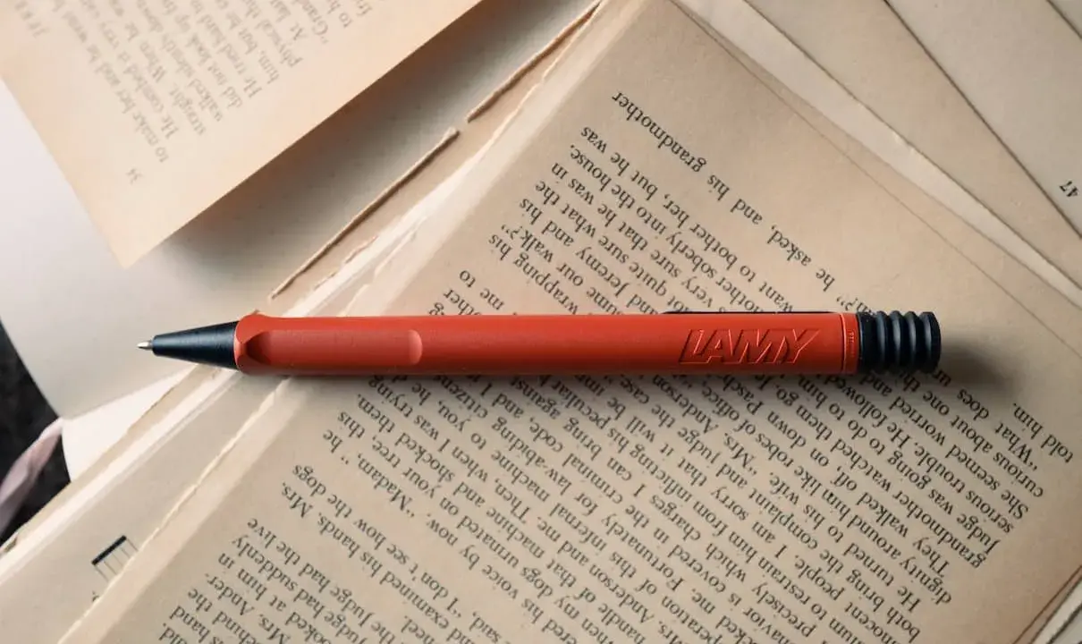 Un stylo rouge Lamy repose sur des pages jaunies. Force est de constater que la lecture et l'écriture font partie de notre histoire.
