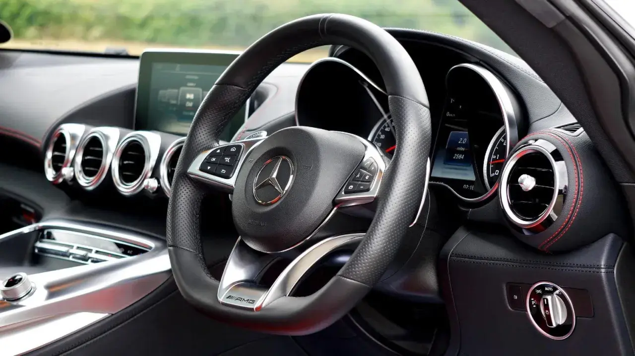 Interior de un coche deportivo Mercedes-AMG. Volante de cuero negro con controles, logo de Mercedes y detalles AMG.