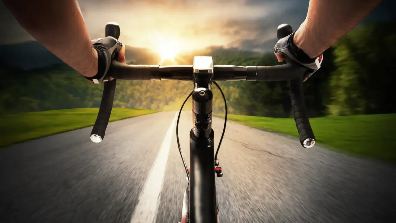 Rowerzysta w rękawiczkach pędzi po asfalcie. Słońce zachodzi, a krajobraz rozmywa się w tle. Ile czasu zajmie mu przejechanie 100 km rowerem?