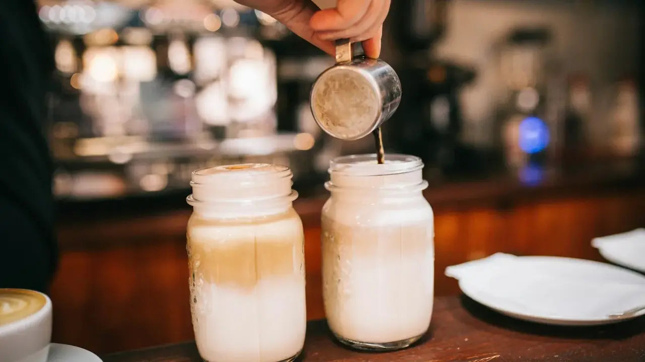 Barista bereitet Latte Macchiato zu. Die Frage "wie viel Kalorien hat ein Latte Macchiato" beschäftigt viele Genießer.
