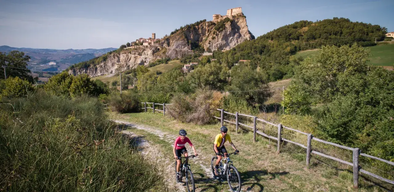 Ciclisti su una ciclabile panoramica con un borgo fortificato in lontananza, un'avventura tra le colline vicino a Rimini.