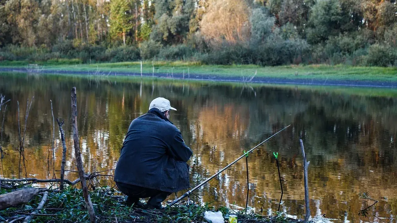 Wędkarz siedzi nad jeziorem, czekając na branie. Na brzegu leży zanęta na tołpyge, gotowa do użycia.