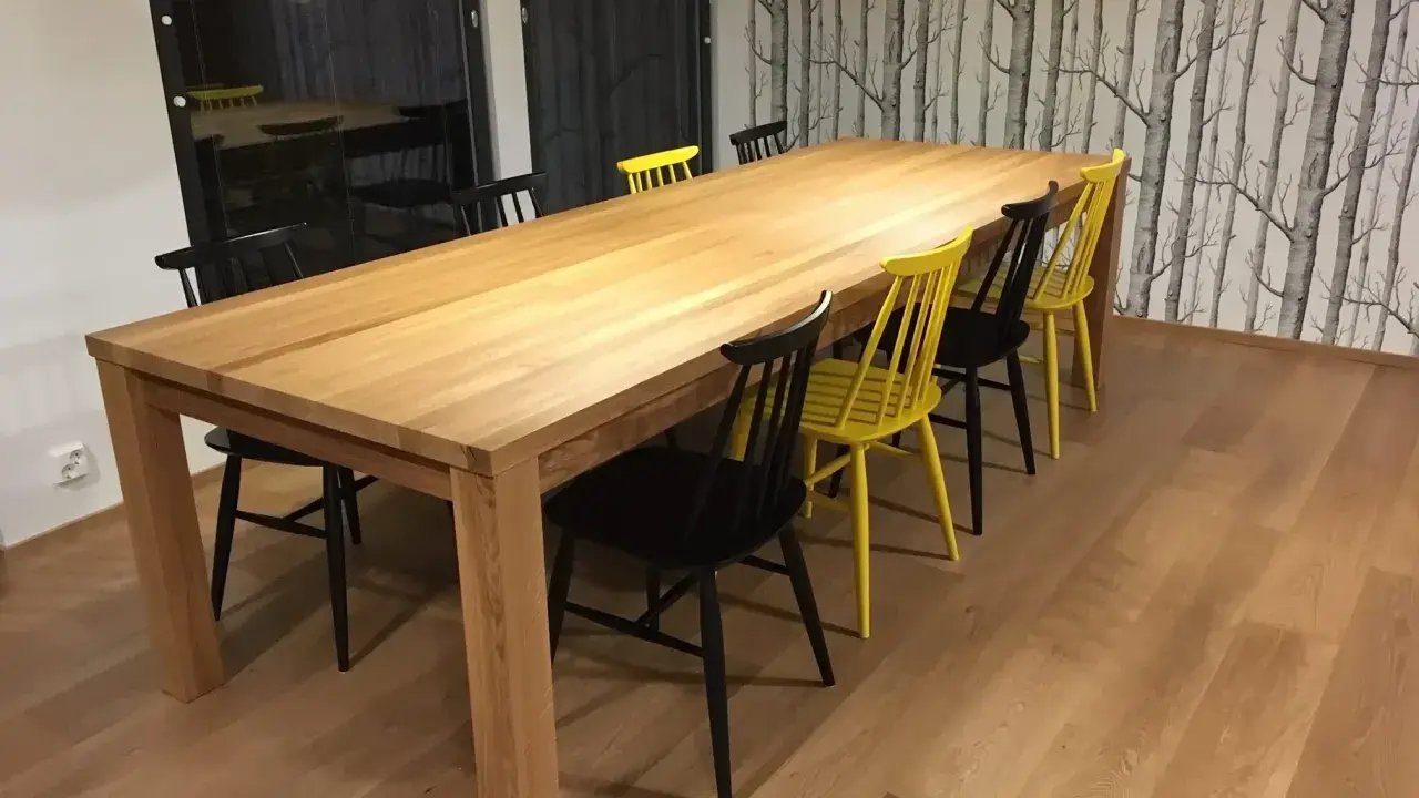 Stilleben matbord i trä med svarta och gula stolar. Bakom syns en fondvägg med trädmotiv.