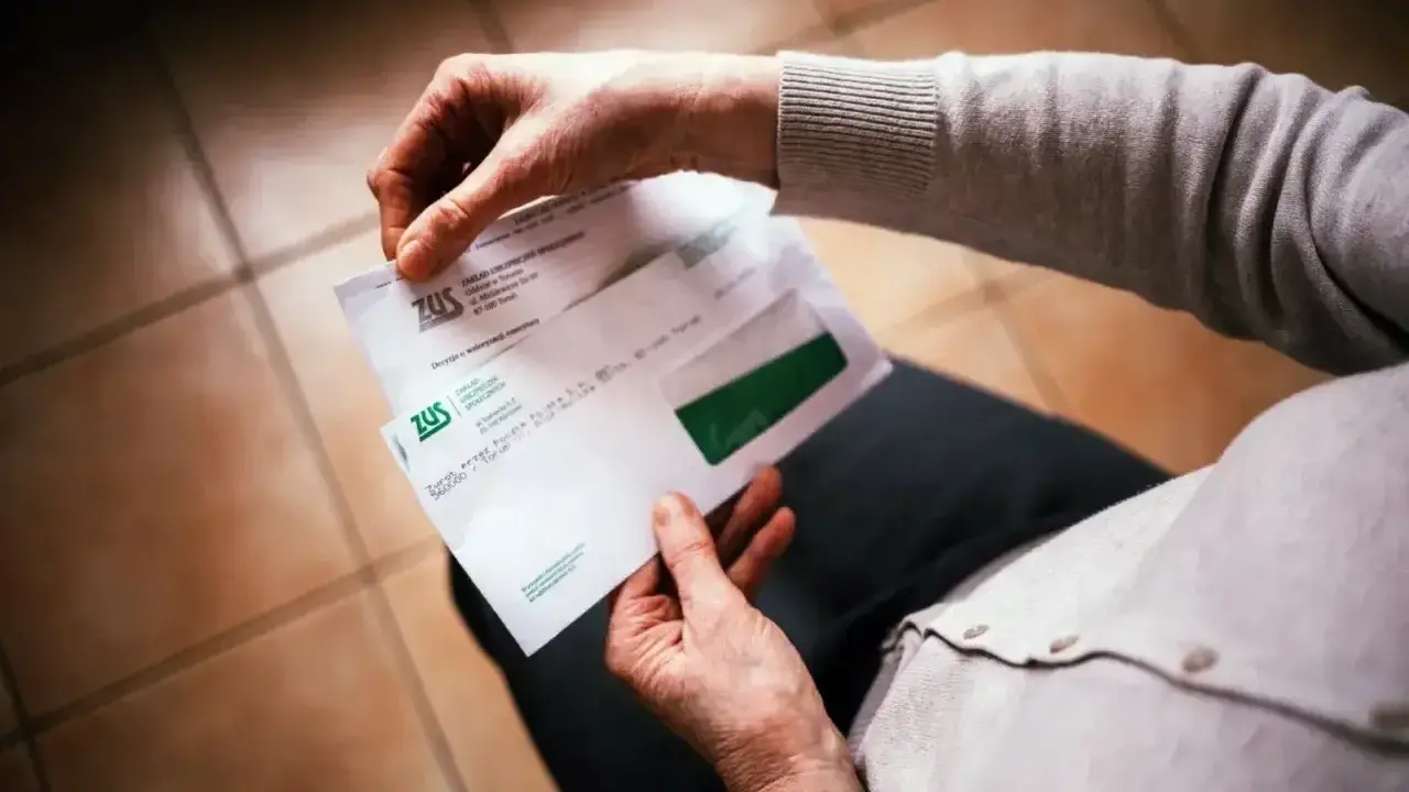 Dłonie trzymają kopertę ZUS. W środku decyzja o waloryzacji emerytury, być może zapowiedź trzynastej emerytury.