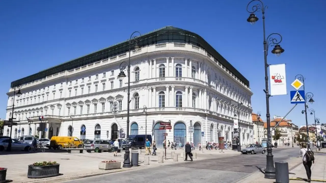 Elegancki, biały budynek w centrum Warszawy, być może najdroższy hotel w Warszawie. Słoneczny dzień, ruch uliczny.
