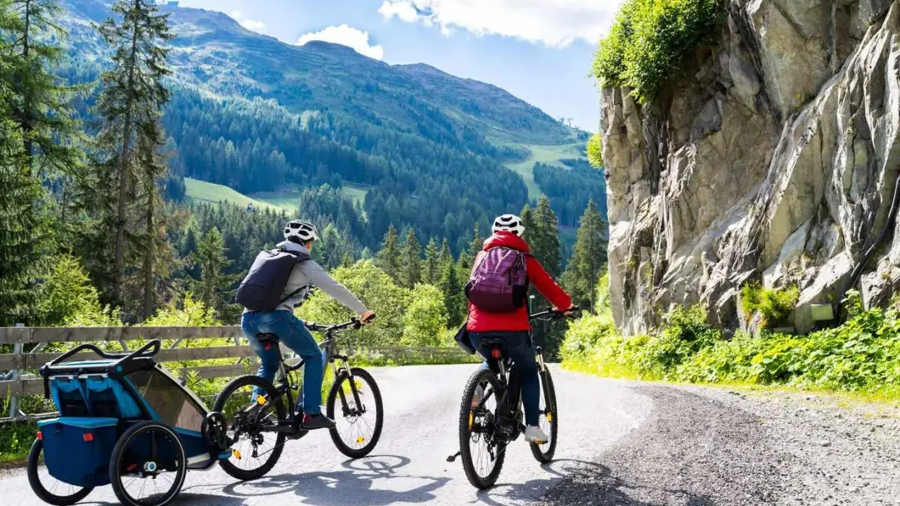 Zwei Radfahrer mit Rucksäcken und Anhänger fahren auf einer Bergstraße.