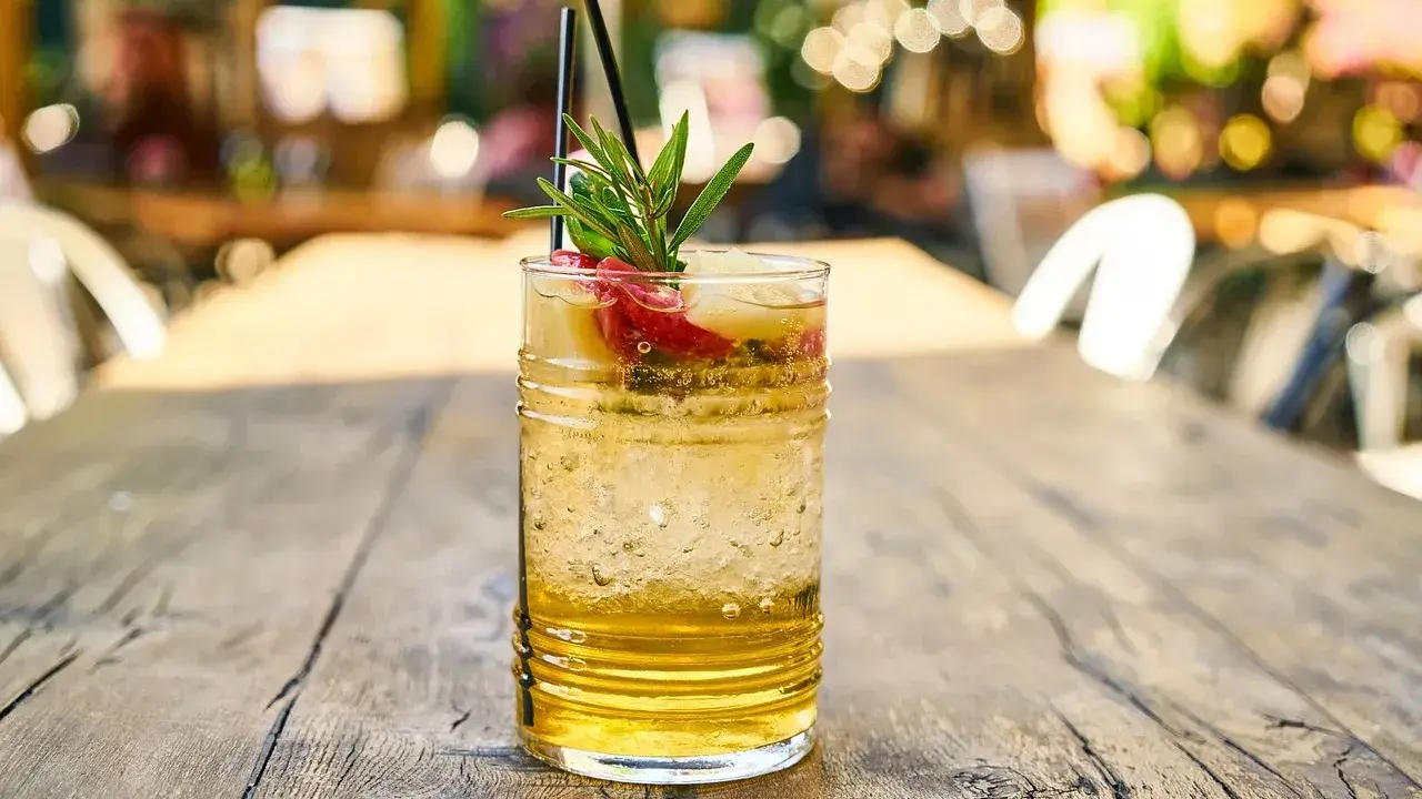 Orzeźwiający drink z wódką waniliową, lodem, owocami i gałązką rozmarynu na drewnianym stole.