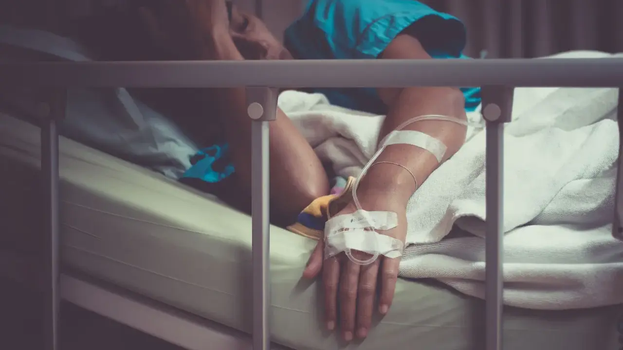 Pacjent w łóżku szpitalnym, z kroplówką, cierpiący. Może to być objaw wstrząsu septycznego, kod ICD-10 A41.