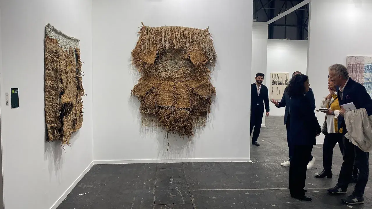 Exhibición de arte contemporáneo con tapices texturizados y personas observando.
