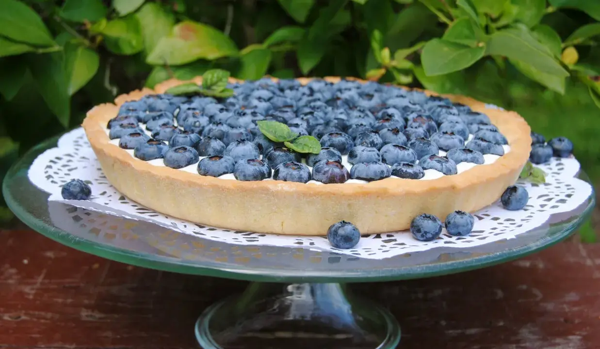 Pyszna tarta z borówkami, udekorowana listkami mięty, prezentuje się apetycznie na szklanej paterze.
