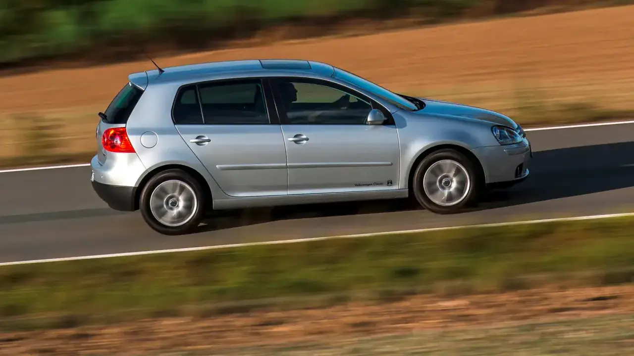 Srebrny Golf 5 1.9 TDI w ruchu, z rozmytym tłem pól i zieleni.