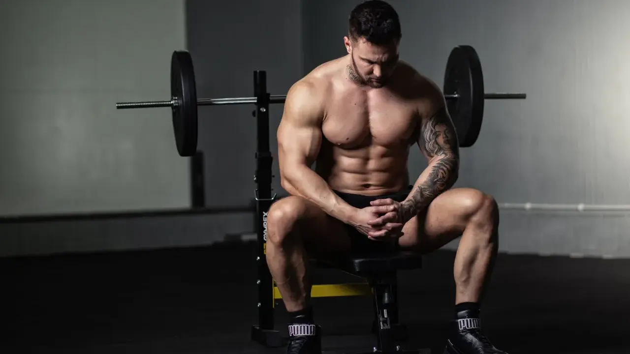 Muskulöser Mann sitzt nach dem Training auf einer Bank, bereit für die Definitionsphase seines Trainingsplans.