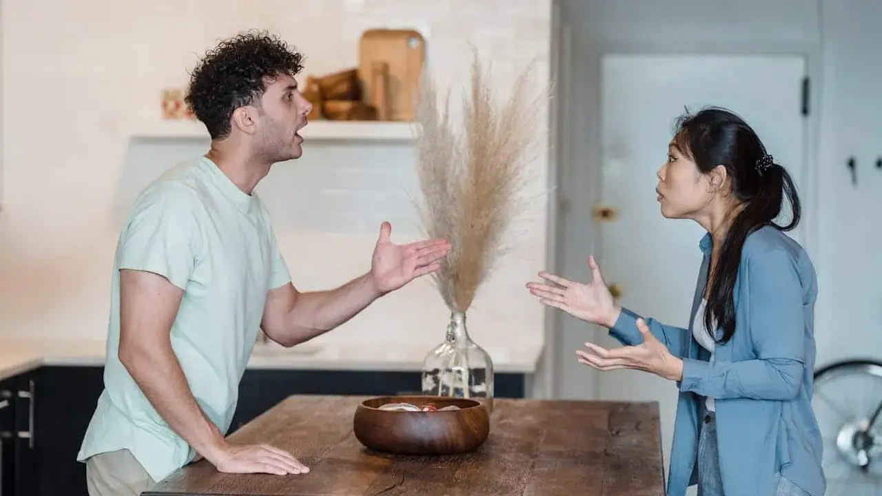 Pareja discutiendo en la cocina, un momento de reflexiones de pareja en crisis. Sus gestos y expresiones muestran tensión.