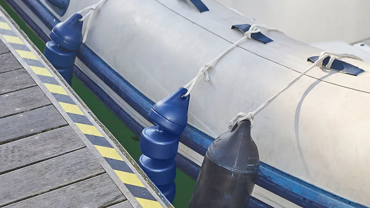 Un bateau pneumatique est amarré à un quai, avec des pare-battages bleus et noirs prêts à gonfler pour protéger la coque.