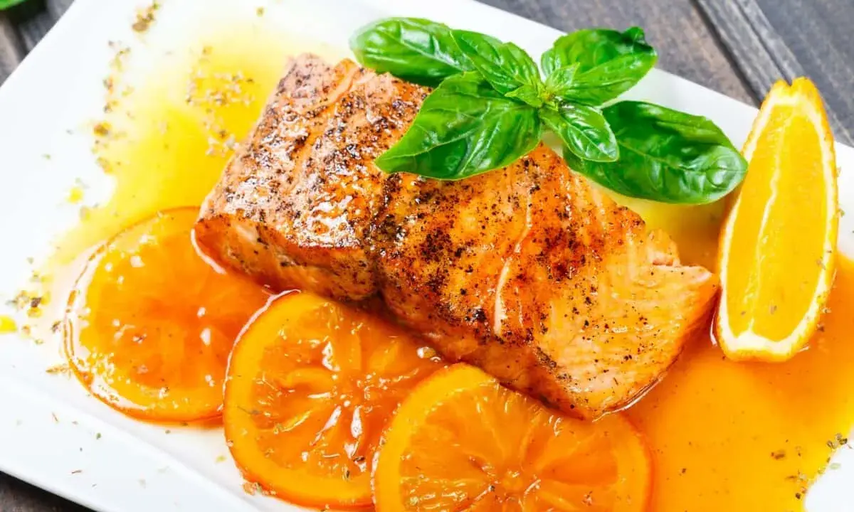 Delicioso salmón a la naranja, jugoso y dorado, servido con rodajas de naranja fresca y una salsa vibrante.