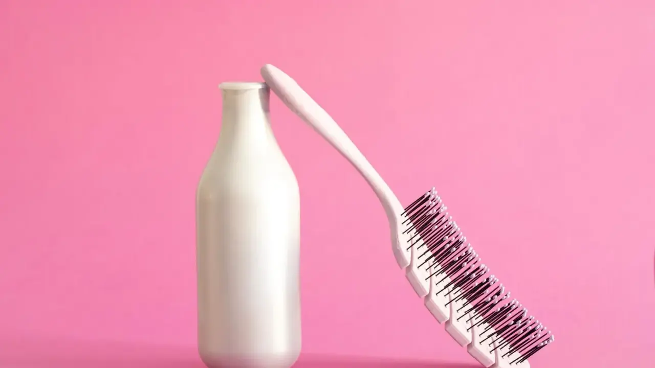 Eine weiße Flasche, die wie ein **collagen shampoo** aussieht, lehnt an einer Haarbürste auf rosa Hintergrund.