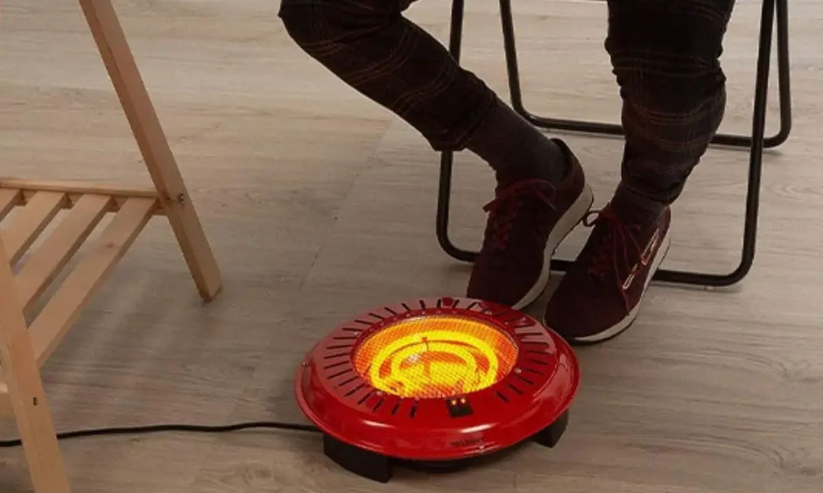 Persona calentando sus pies con un brasero eléctrico rojo bajo un escritorio.