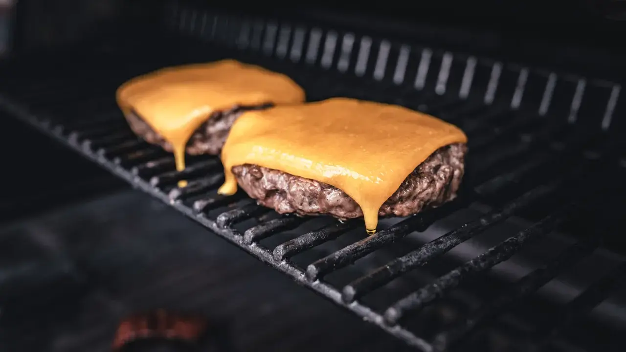 Zwei saftige Burger-Patties auf dem Grill, mit leckerem cheddar schmelzen, der langsam heruntertropft.