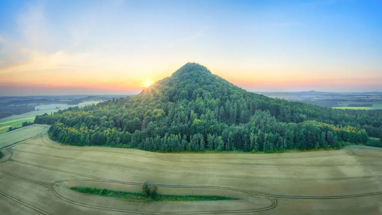 Góry Kaczawskie o wschodzie słońca. Zielony, zalesiony stożek wznosi się nad polami.