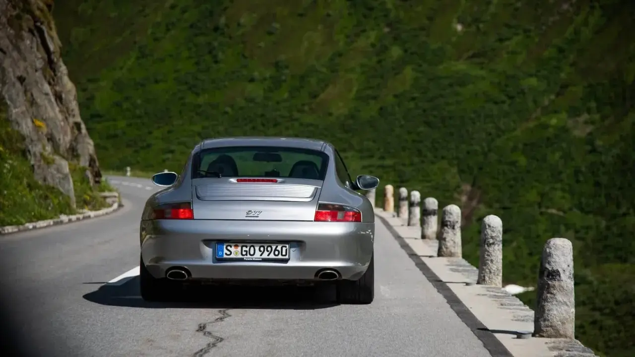 Silberner Porsche 996 4S auf Bergstraße. Ein Klassiker mit Potenzial für Wertsteigerung, der die Freiheit der Fahrt genießt.