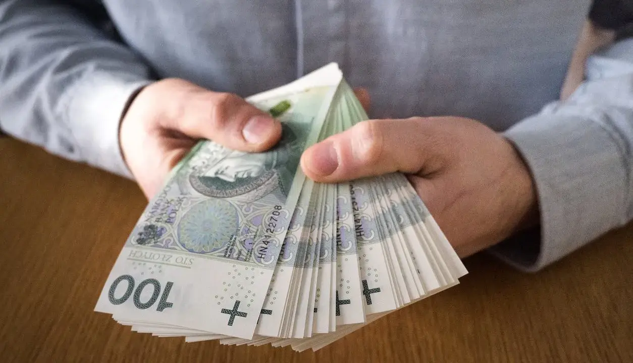 Dłonie trzymające plik banknotów 100 zł. Symbolizuje to zarobki, które mogą być wynikiem najlepiej płatnych zawodów.