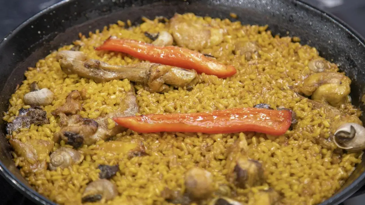 Paella de arroz con carne, pimientos rojos y caracoles. Un plato tradicional español lleno de sabor.