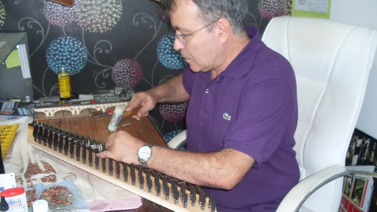 Un artisan ajuste les cordes d'un kanun, instrument de musique traditionnel, avec un marteau.