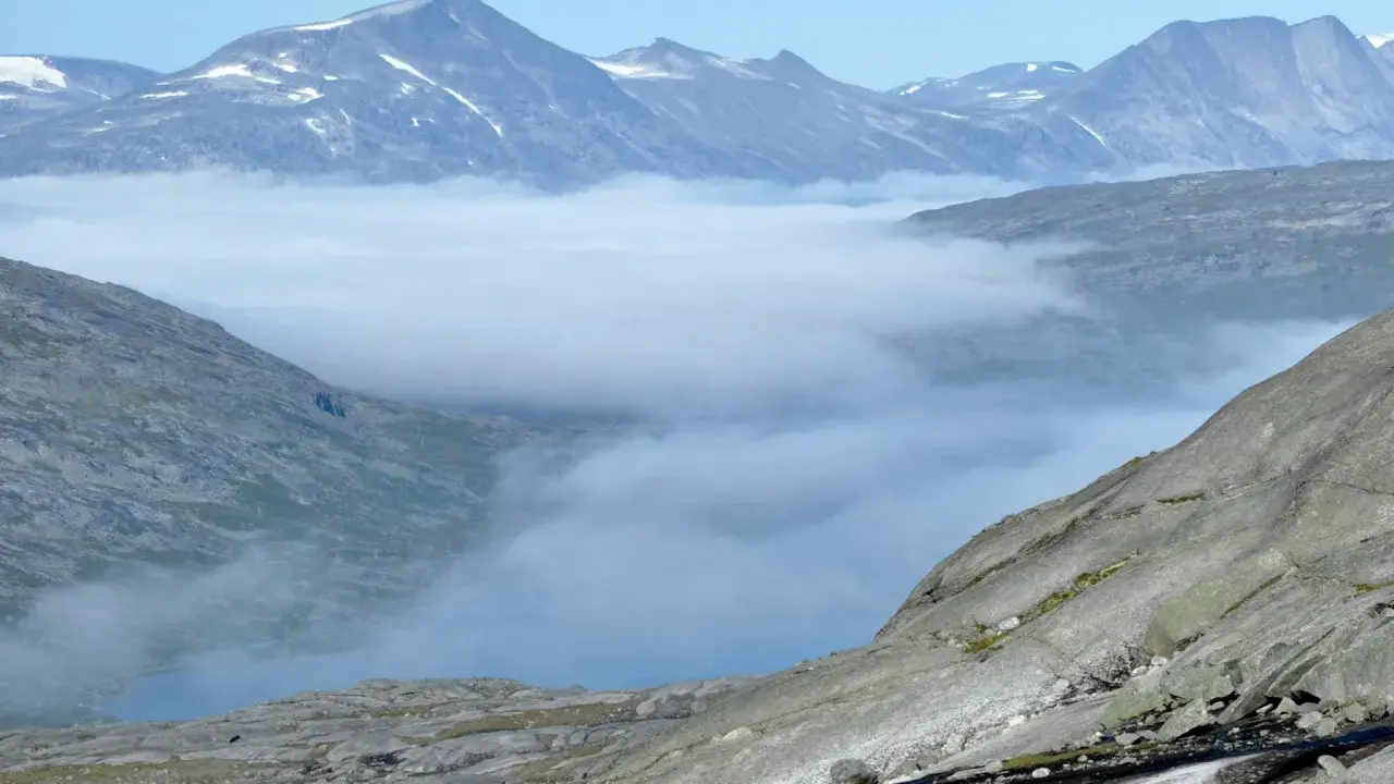 Moln sveper genom dalarna i Padjelanta nationalpark, med snöklädda bergstoppar som reser sig mot en klarblå himmel.