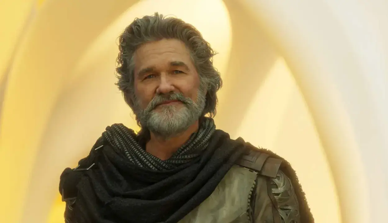 Kurt Russell som Ego i filmer med kurt russell, med grått hår och skägg, klädd i en mörk sjal och rustning mot en gul bakgrund.