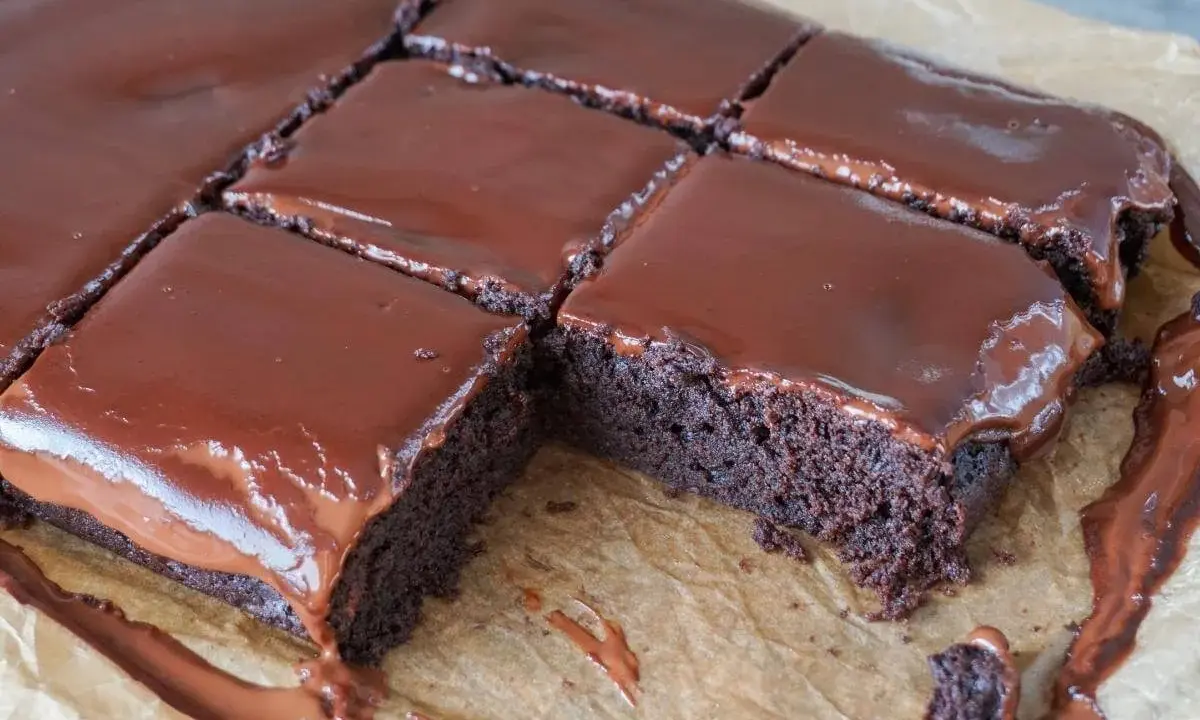 Saftige, vegane Brownies mit glänzendem Schokoladenguss, auf Backpapier zugeschnitten. Ein Traum für jeden Schokoladenliebhaber!