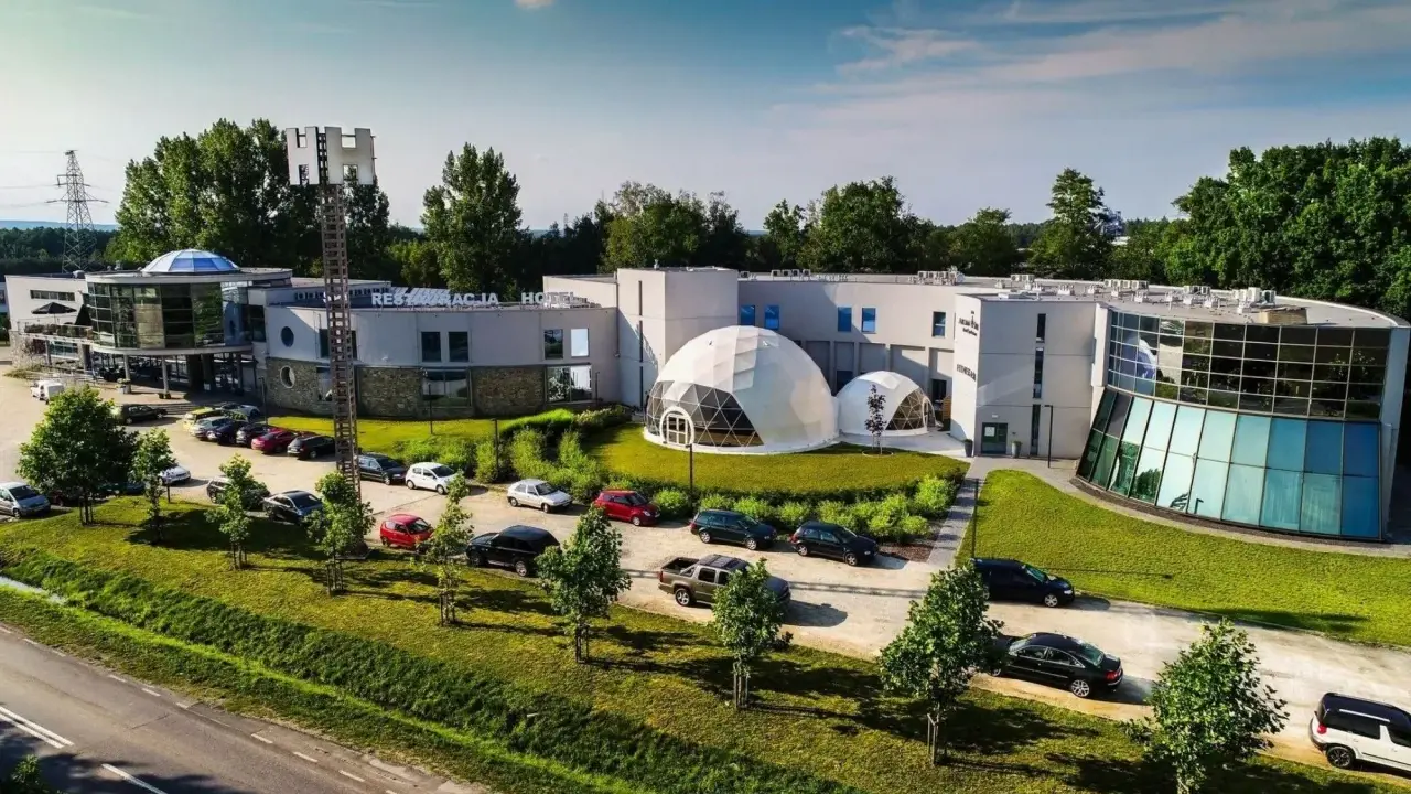 Nowoczesne polskie hotele niezależne z kopułami i przeszklonymi fasadami, otoczone zielenią i parkingiem pełnym samochodów.