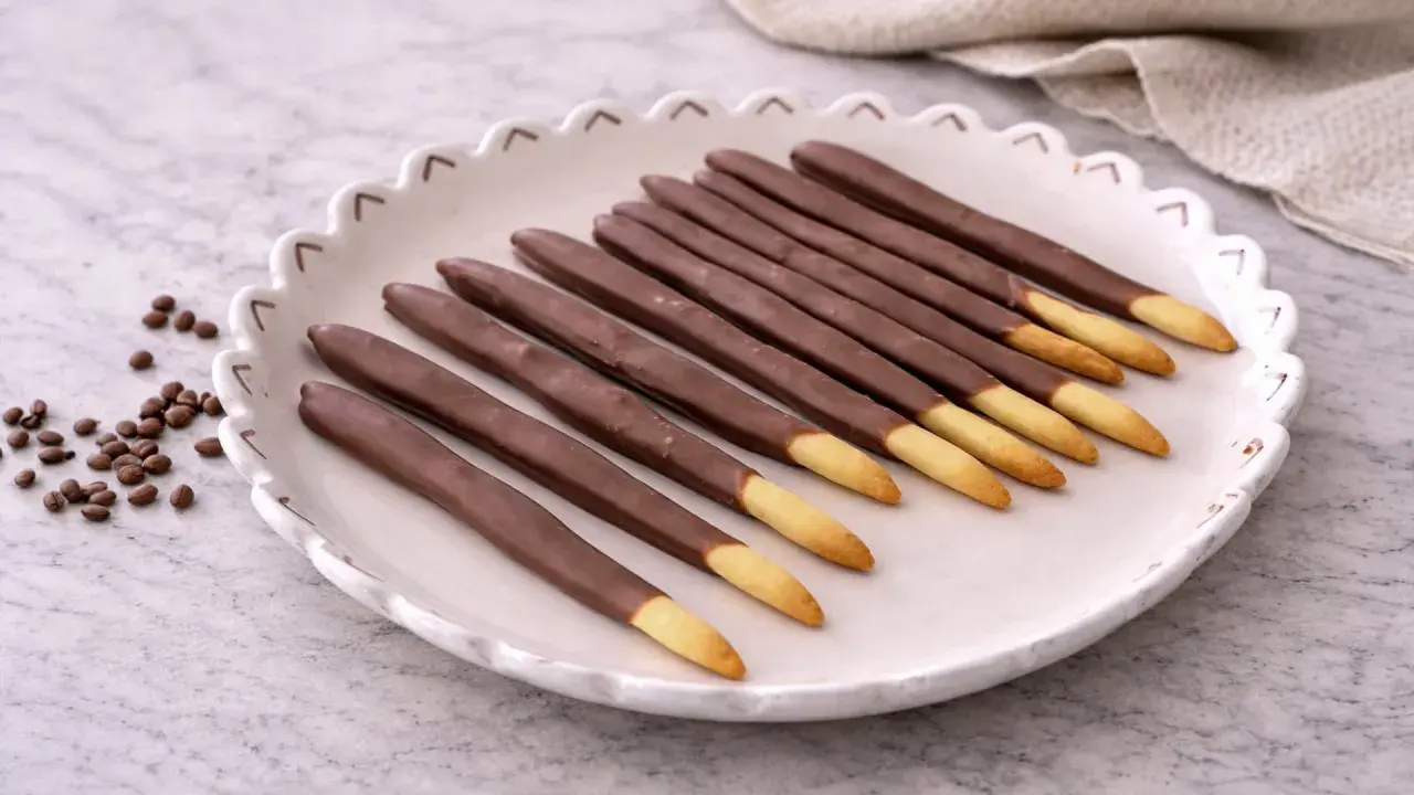 Assiette de mikado maison, bâtonnets de biscuit enrobés de chocolat, avec quelques grains de café à côté.