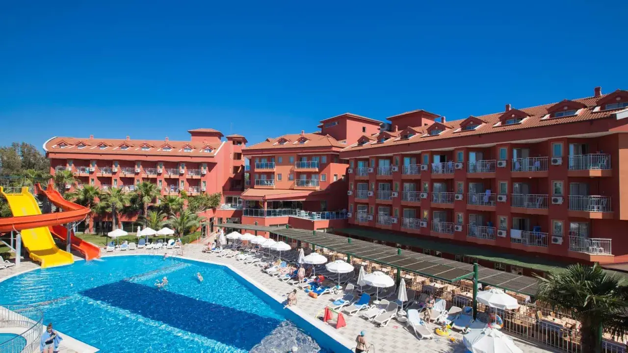 Słoneczny dzień w club side coast. Basen z wodnymi zjeżdżalniami, leżaki i palmy przy hotelu.