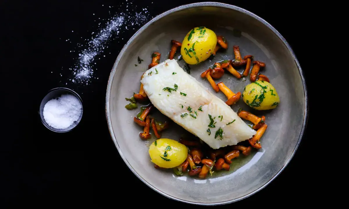 Ein köstliches Heilbutt-Rezept: zartes Fischfilet mit kleinen Kartoffeln und Pfifferlingen, garniert mit frischen Kräutern.
