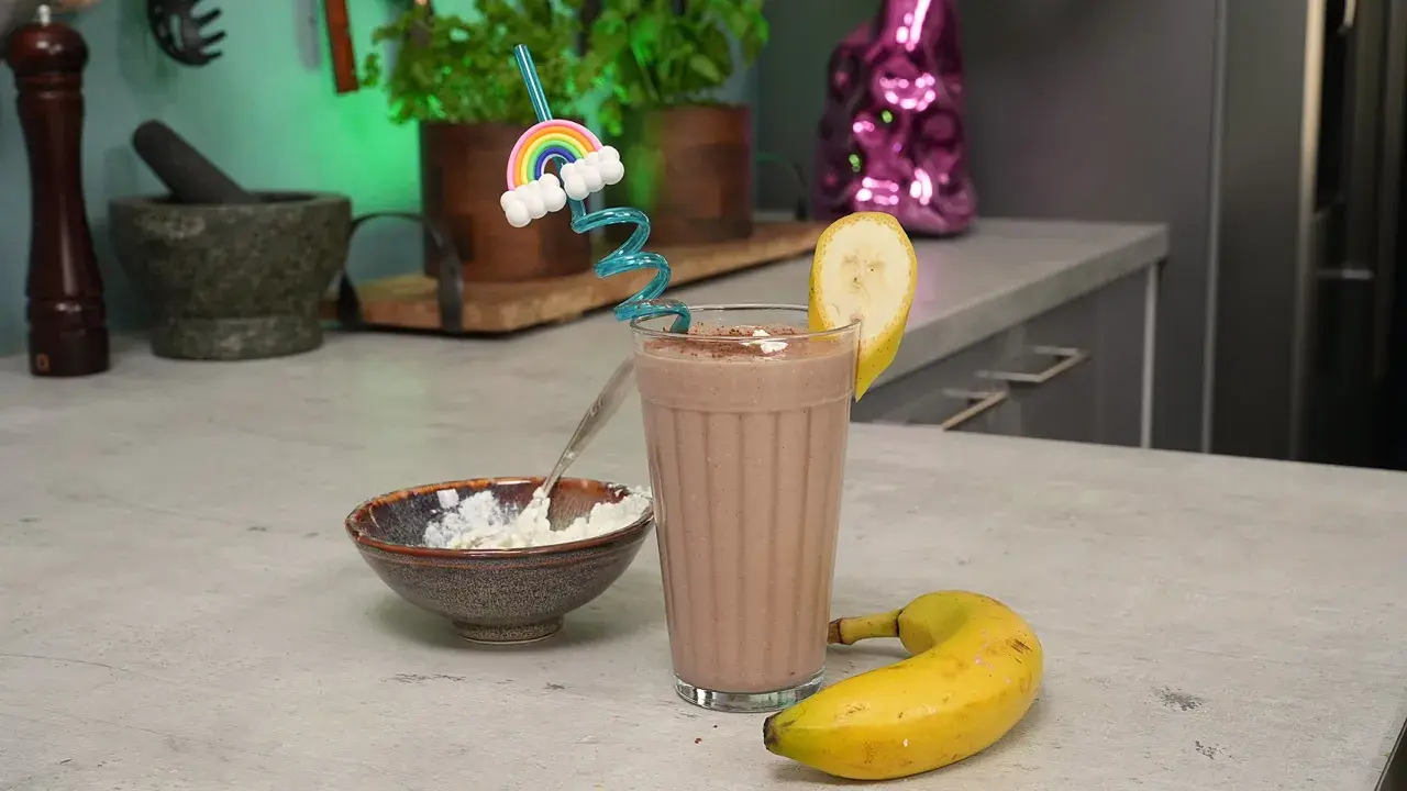Ein leckerer schoko protein shake mit Banane und einem lustigen Regenbogen-Strohhalm. Daneben eine Schale mit Quark.