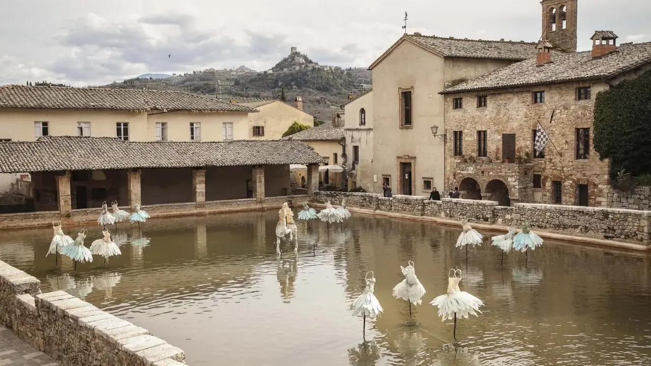 Bagno Vignoni: cosa vedere? La vasca termale con installazioni artistiche di abiti da ballo e un cavallo bianco.