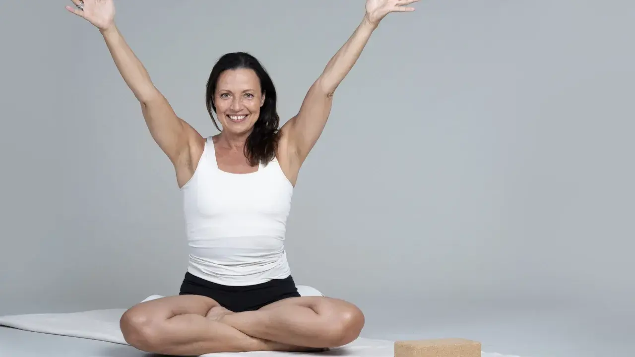 Kvinna i meditationsställning med armarna uppåt, utstrålar lugn och glädje. Hon praktiserar metta meditation för inre frid.
