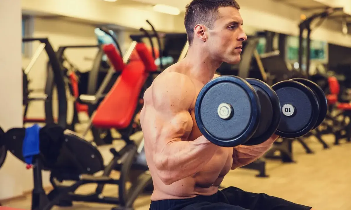 Hombre concentrado realizando ejercicios de bíceps con mancuernas en el gimnasio.
