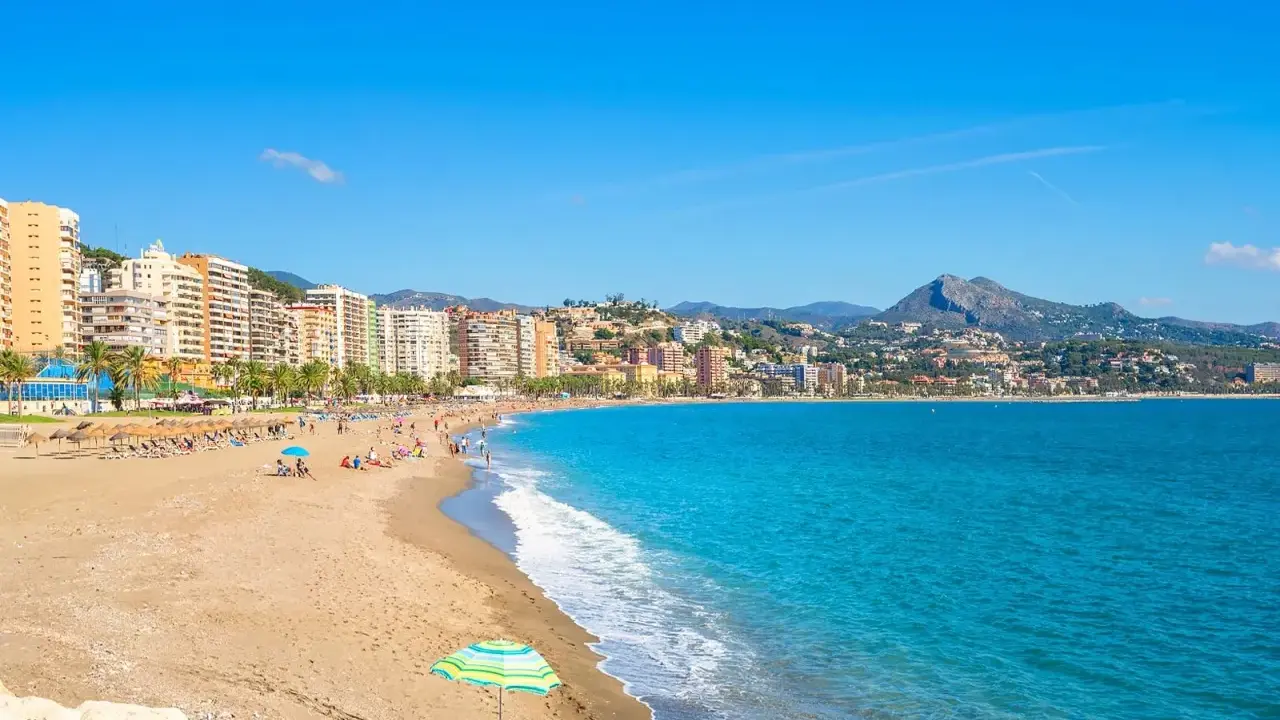 En solig dag på malaga strand med turkost vatten, sand och en stadskant i bakgrunden. En perfekt plats för avkoppling.