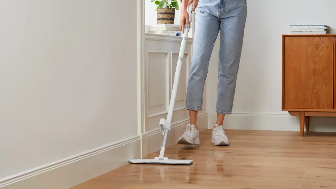 Person wischt den Holzboden, um die Wohnung zu reinigen. Ein moderner Wischmopp gleitet über das glänzende Parkett.